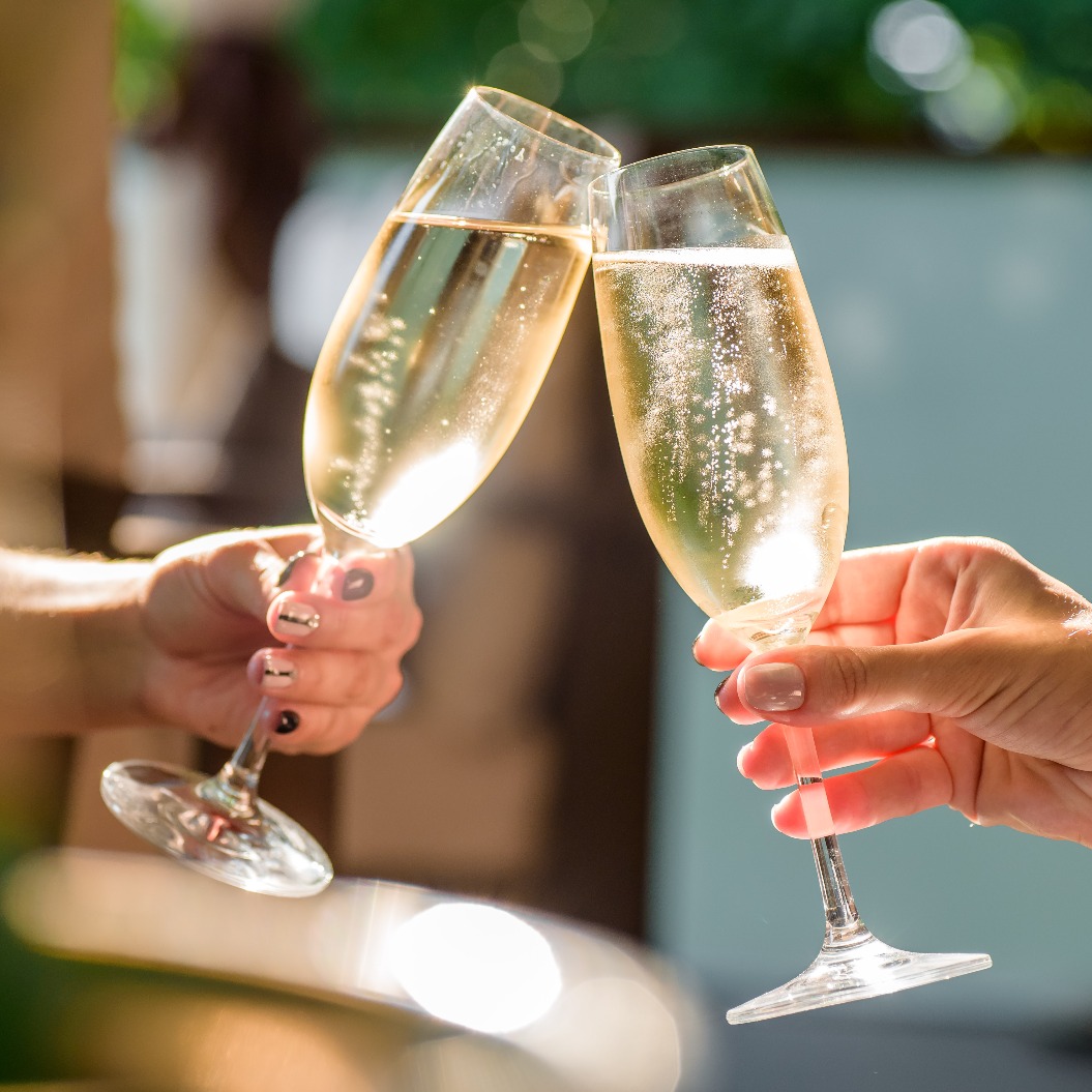 Zwei Mädchen stoßen auf einer schönen Sommerterrasse mit Champagner an. Prickelnde Champagnergläser
